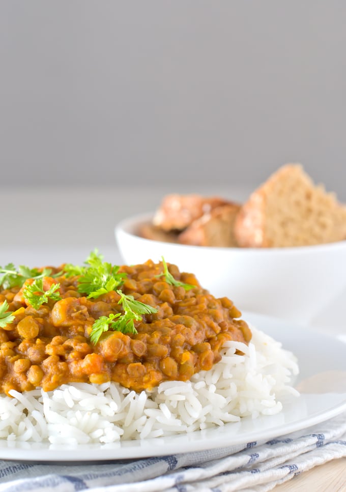 Photo of a plate with some vegan lentil curry over white rice and garnished with fresh parsley.