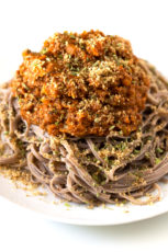 Photo of a dish of vegan bolognese with some pasta and vegan Parmesan cheese.