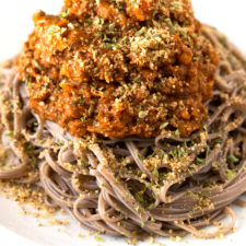 Photo of a dish of vegan bolognese with some pasta and vegan Parmesan cheese.