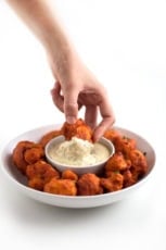 Photo of a plate of buffalo cauliflower wings being dipped in vegan ranch dressing