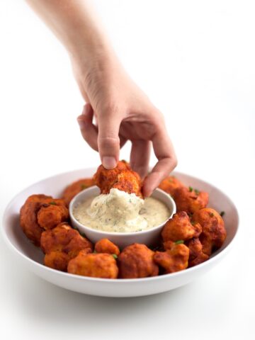 Photo of a plate of buffalo cauliflower wings being dipped in vegan ranch dressing