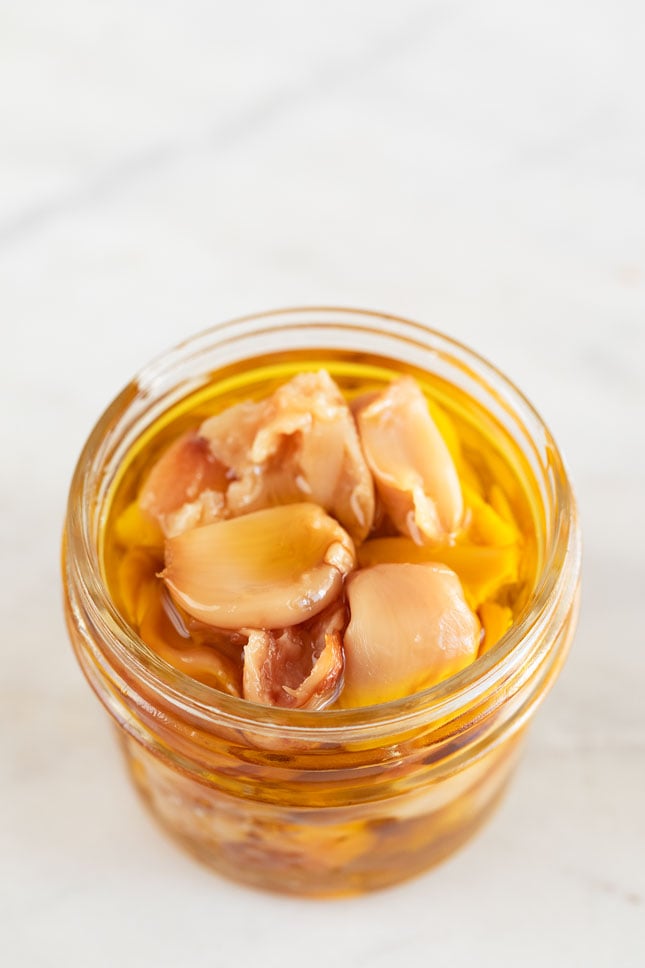 A small glass container with roasted garlic cloves and covered with extra virgin olive oil