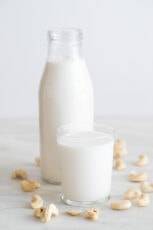 A side shot of a bottle and a glass with cashew milk