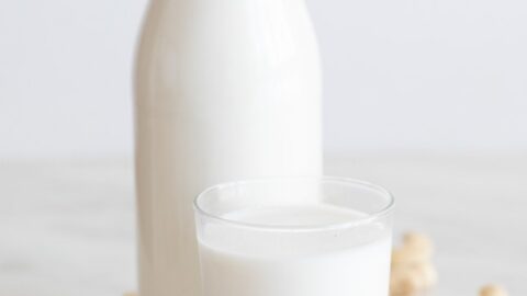 A side shot of a bottle and a glass with cashew milk