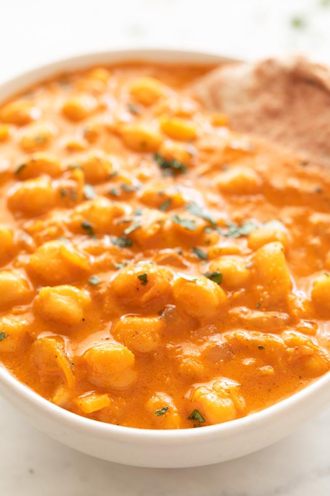 Close-up shot of a bowl of chickpea curry decorated with some bread