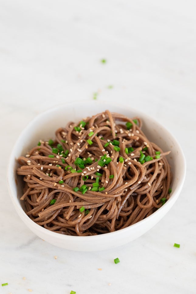 A picture of a bowl with sesame noodles garnished with sesame seeds and fresh parsley