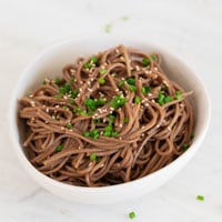 A square picture of a bowl with sesame noodles garnished with sesame seeds and fresh parsley