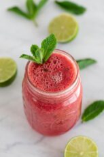 Photo of a jar of watermelon smoothie with mint leaves and sliced lime as decoration