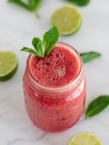 Photo of a jar of watermelon smoothie with mint leaves and sliced lime as decoration