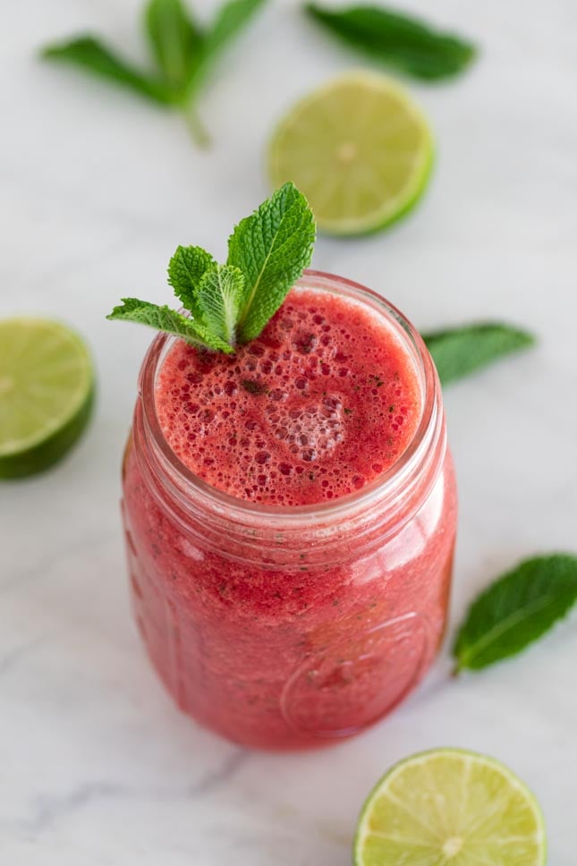 Jar of watermelon smoothie decorated with mint leaves and sliced lime