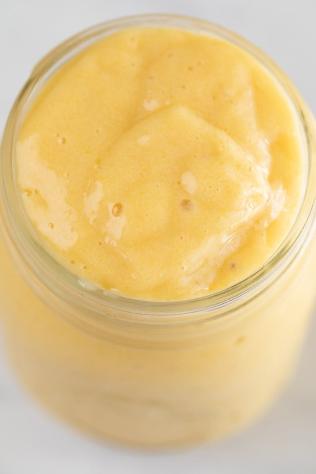 A close shot of a glass container with a super creamy mango smoothie