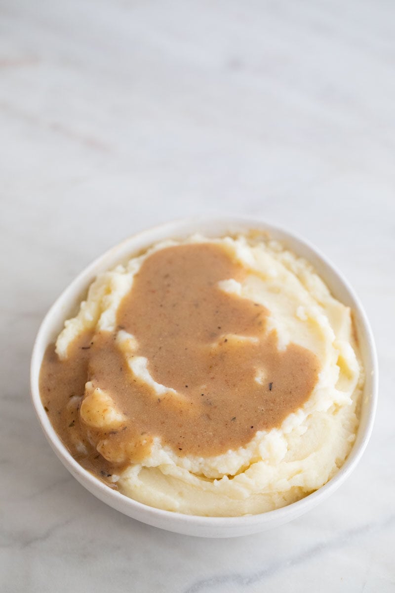 A photo of a small bowl with vegan mashed potatoes topped with some vegan gravy