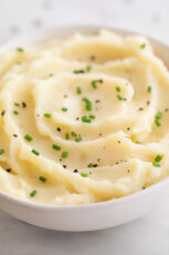 A close shot of a bowl with vegan mashed potatoes with a garnish of chives and pepper
