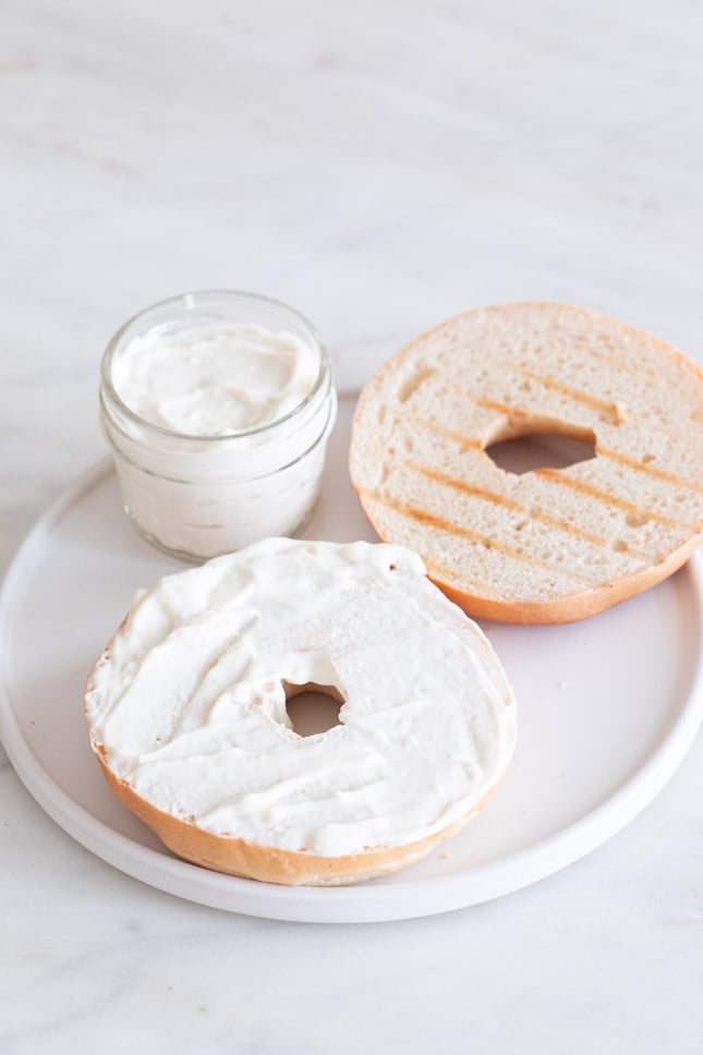 A picture of a dish with a slice bagel spread with vegan cream cheese on top