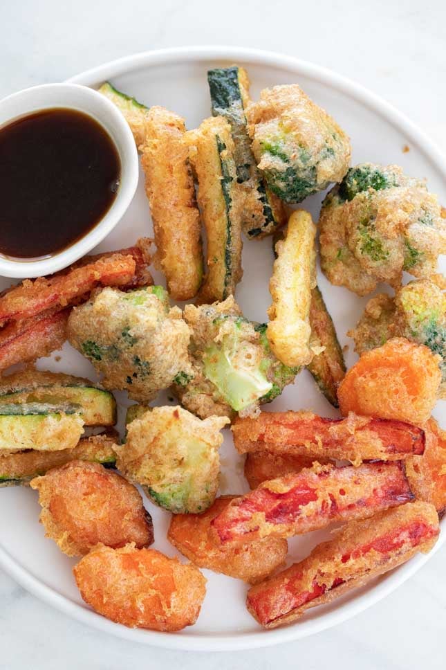 An overhead shot of a dish with homemade vegetable tempura and soy sauce in a bowl
