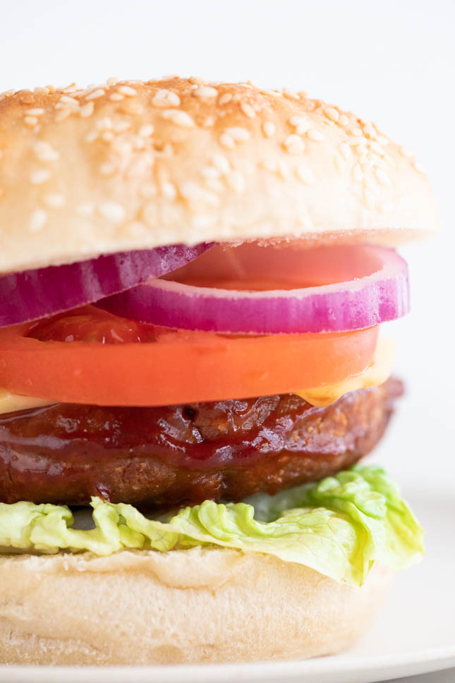 A close shot of a vegan burger with burger bun, lettuce, tomato slices, and red onion onto a dish