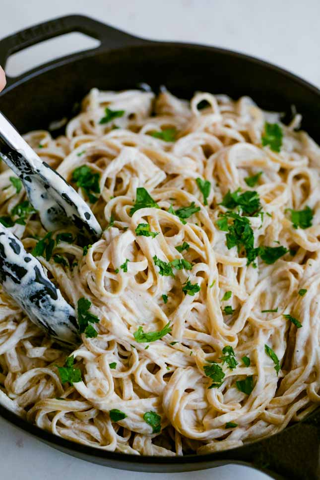 A skillet with vegan Alfredo sauce mixed with cooked spaghetti