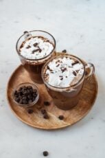 A picture of 2 glass jars with vegan hot chocolate topped with whipped cream and chopped dark chocolate