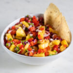 A square picture of a bowl of pineapple salsa with tortilla chips