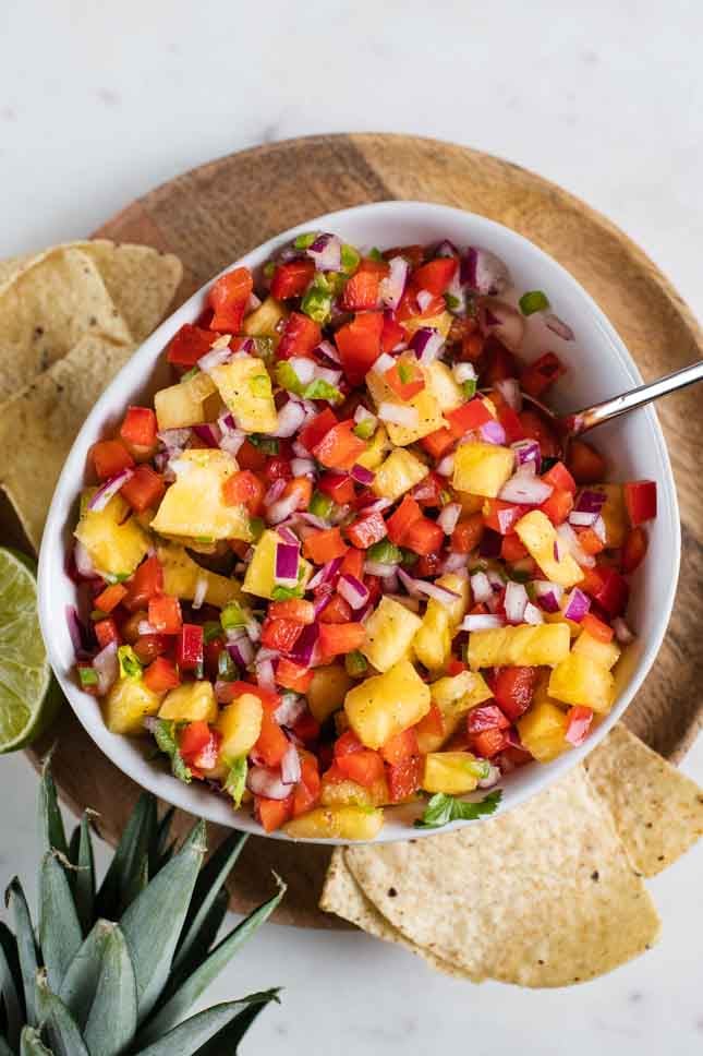 An overhead shot of a bowl of pineapple salsa with tortilla chips and a pineapple
