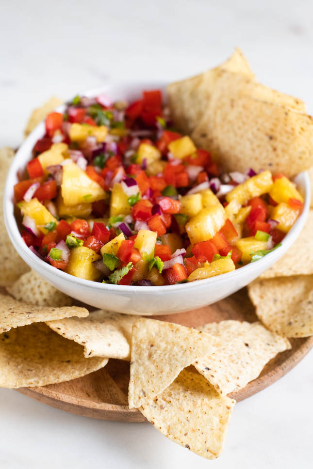 A picture of a bowl of pineapple salsa onto a wooden dish with nachos