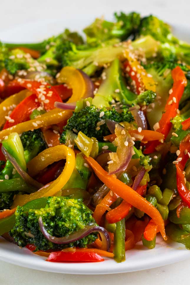 A close shot of a dish with veggie stir fry topped with sesame seeds