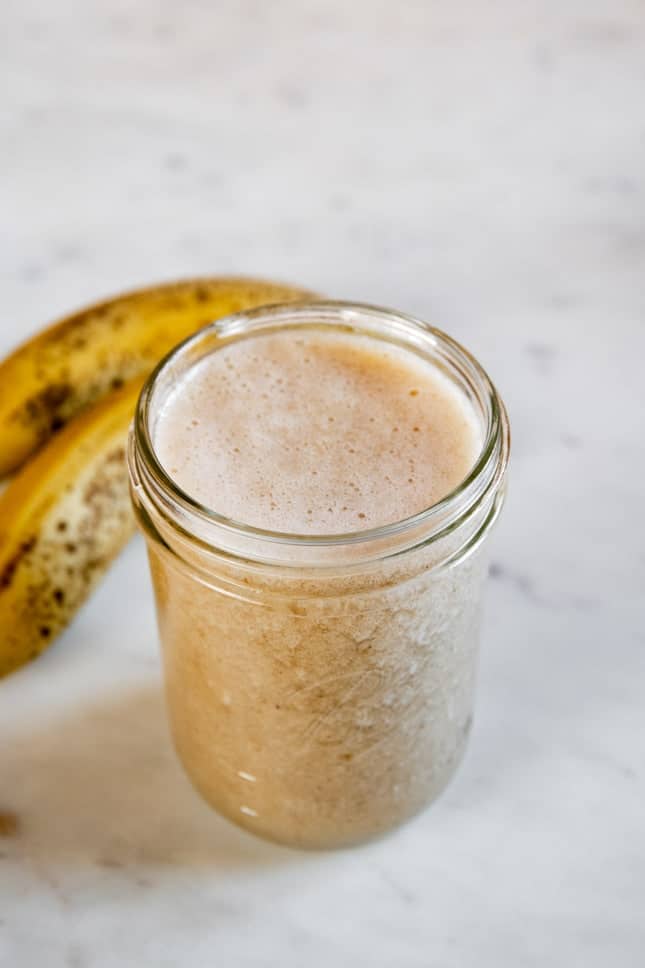 A picture of a couple bananas and a jar with homemade banana milk