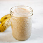 A square picture of a couple bananas and a jar with homemade banana milk