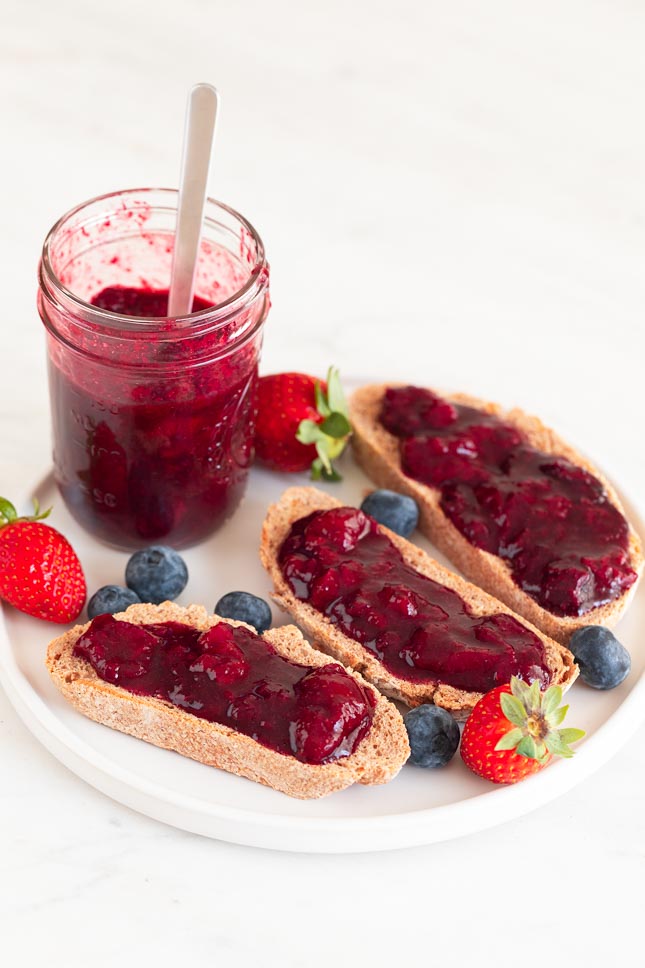 A picture of a jar and some bread slices with berry compote onto a dish