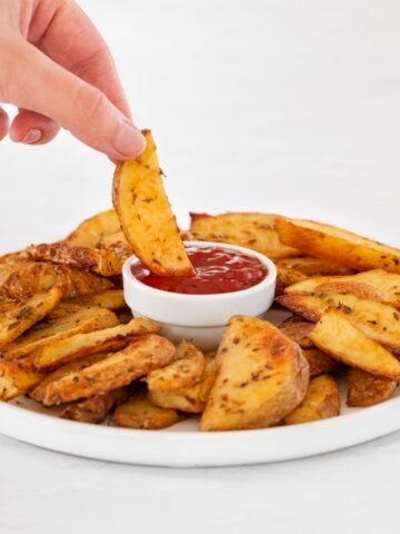 Photo of a potato wedge being dipped in homemade ketchup