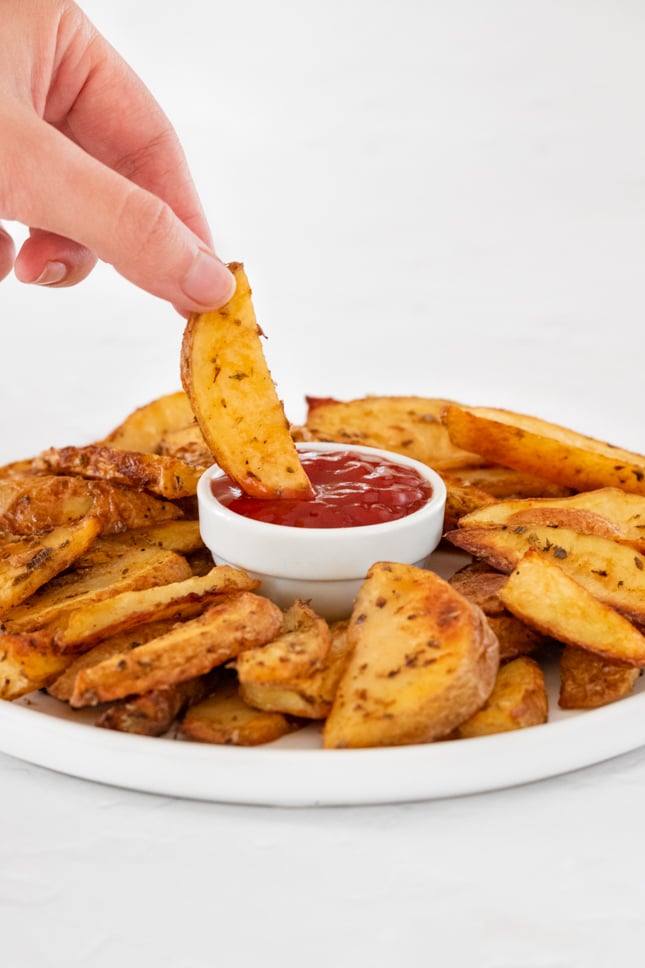 Photo of a potato wedge being dipped in ketchup