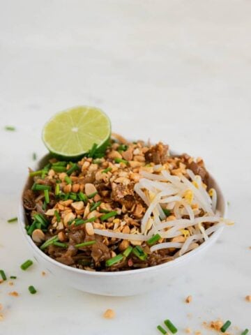 A picture of a bowl of vegan pad Thai with a sliced lime on top