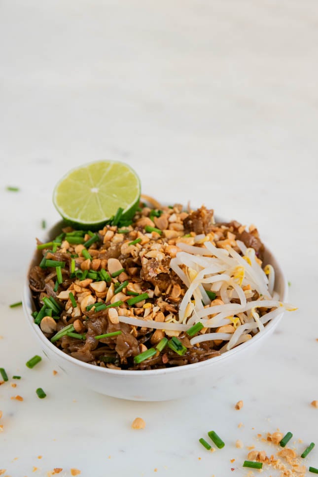 A picture of a bowl of vegan pad Thai with a sliced lime on top