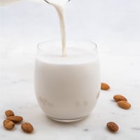 Square photo of a jar pouring almond milk into a glass