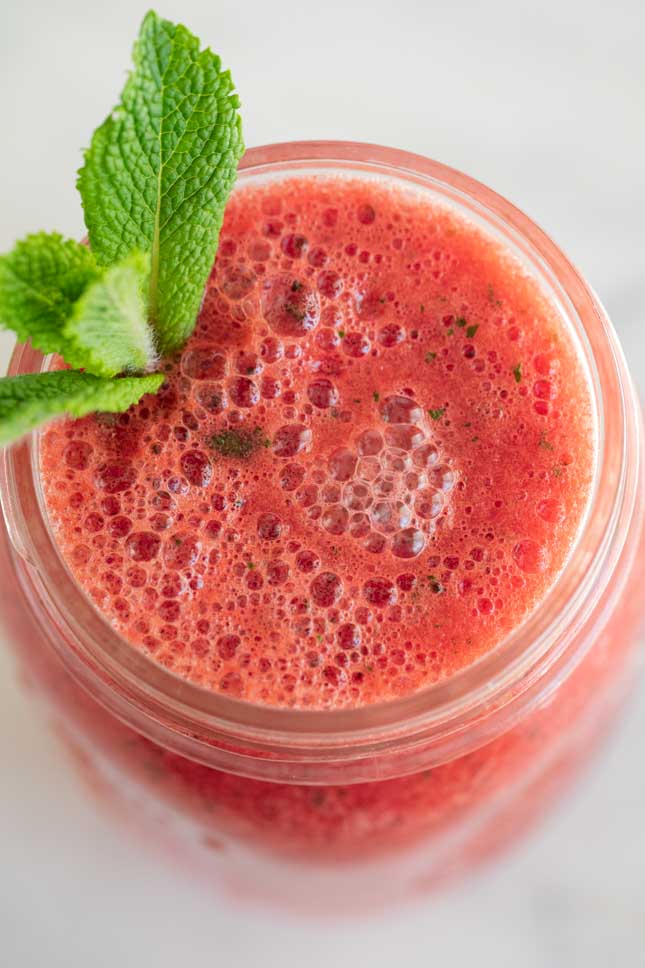 Close-up shot of a jar of watermelon smoothie decorated with some leaves
