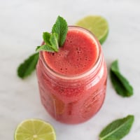 Square photo of a jar of watermelon smoothie decorated with mint leaves and sliced lime