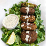 Square photo of a plate of falafel over some greens and vegan yogurt sauce on top