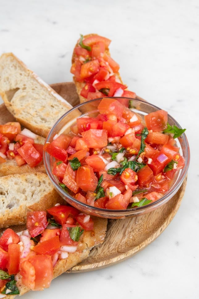 Photo of a plate with some slices of bread with bruschetta mixture in a bowl