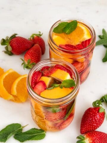 Photo of 2 glass jars of fruit infused water decorated with some fruits