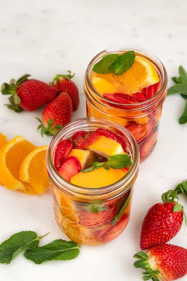 Photo of 2 glass jars of fruit infused water decorated with strawberries, oranges, and mint leaves