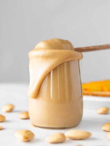 Side shot of a glass of almond butter with a honey spoon in it