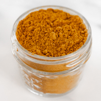 Square photo of a small glass jar of curry powder