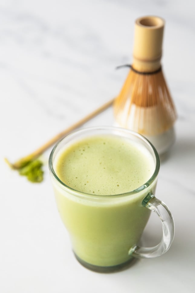 Photo of a cup of matcha latte with a bamboo whisk on the side