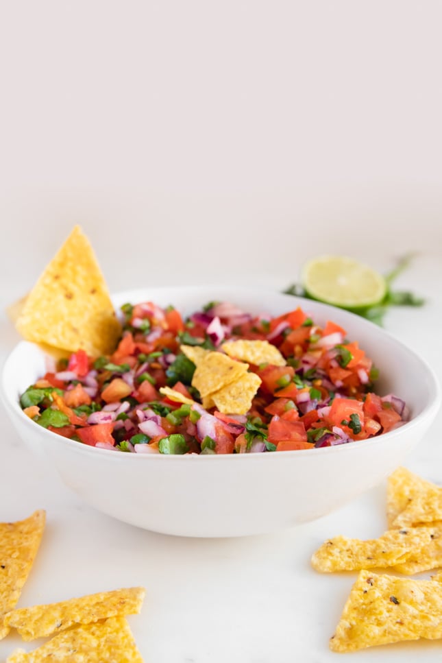 Side shot of a bowl of pico de gallo with some tortilla chips