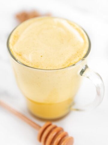 Photo of a glass cup of turmeric latte with a honey spoon