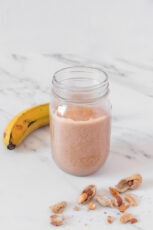 Photo of a glass jar of vegan protein shake decorated with peanuts and a banana