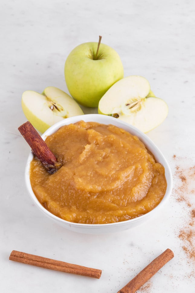 Photo of a bowl of applesauce with some cinnamon sticks and apples as decoration