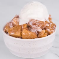 Square photo of a bowl of baked apples and vegan vanilla ice cream