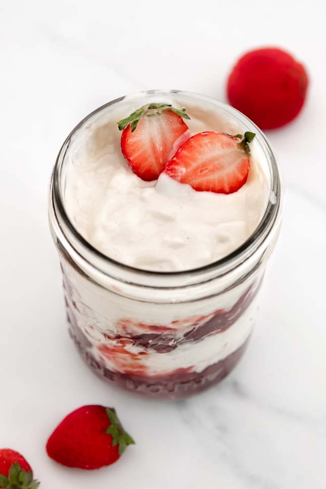 Photo of a glass jar of coconut yogurt with some strawberries