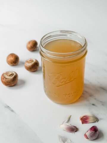 Photo of a glass jar of vegetable stock decorated with some mushrooms